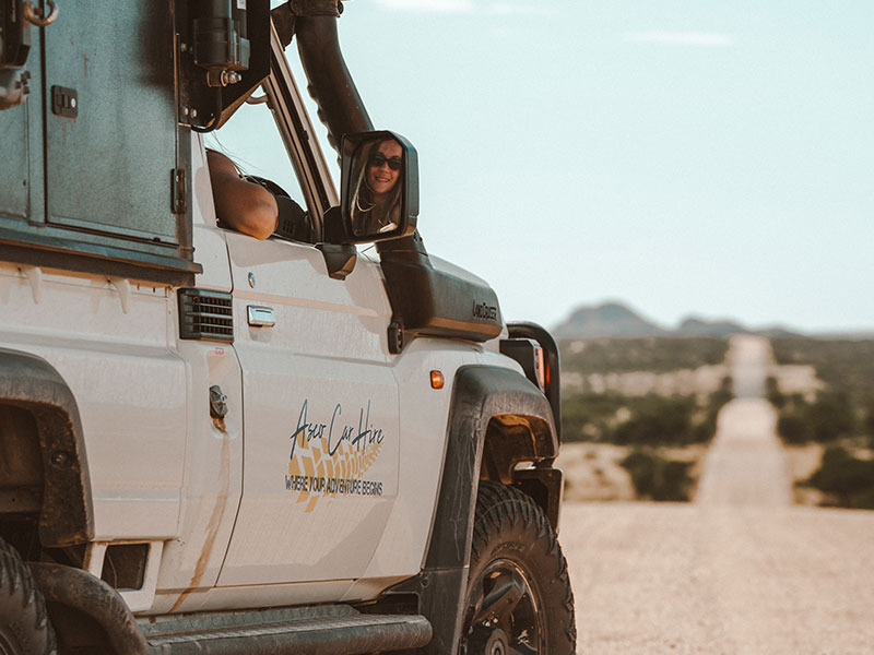 4x4-huurauto voor een self-drive-avontuur, met geopende daktent en een reiziger die uit het autoraam hangt
