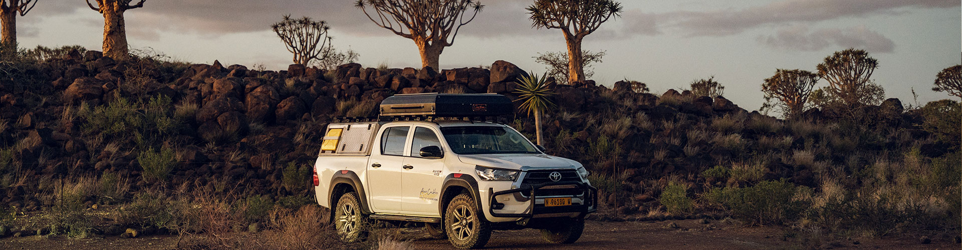Asco Car Hire Toyota Hilux offroad in een karakteristiek Namibisch landschap met kokerbomen op de achtergrond