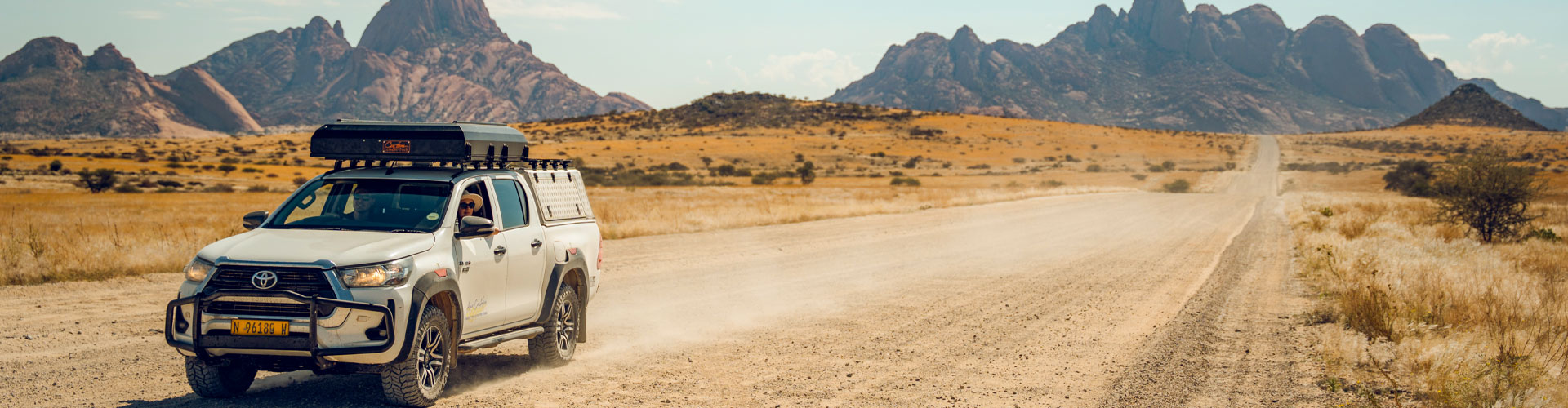 Asco Toyota Hilux 4x4 with rooftop tent driving on a dirt road through Namibian desert landscape