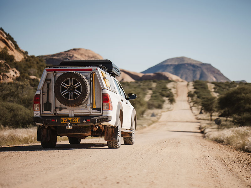 Toyota Hilux 4x4 met daktent, rijdend over een onverharde weg door het woestijnlandschap van Namibi&euml;
