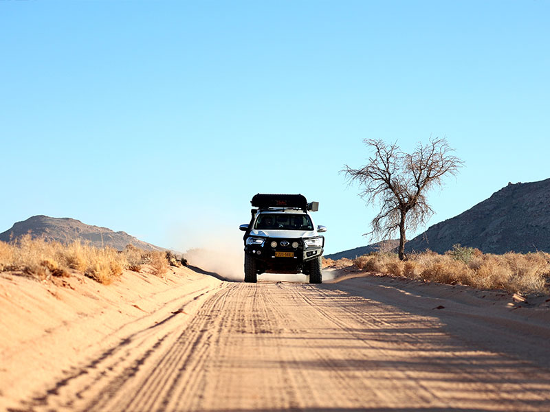  Toyota Hilux 4x4 mit Dachzelt, unterwegs auf einer Schotterstra&szlig;e durch die W&uuml;stenlandschaft Namibias