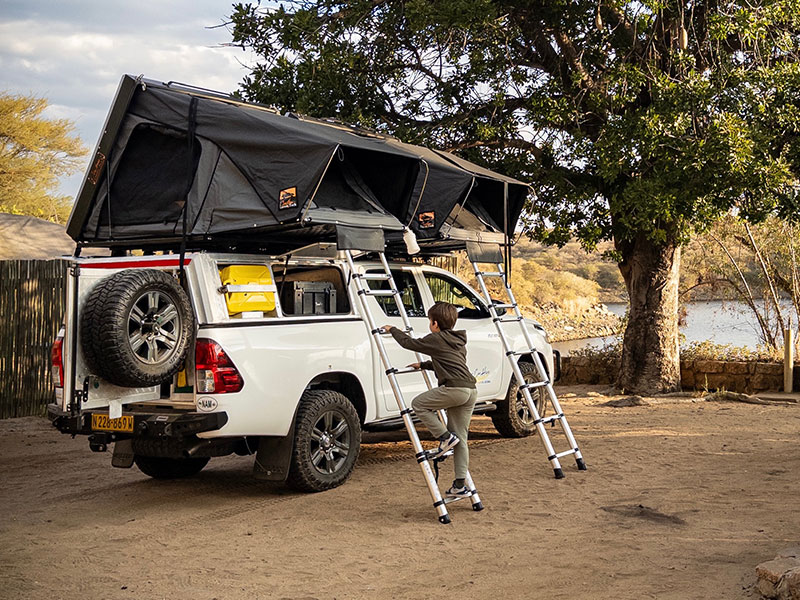 Child climbing a ladder to access Asco 4x4 Car Rental equipped with rooftop tent and camping gear