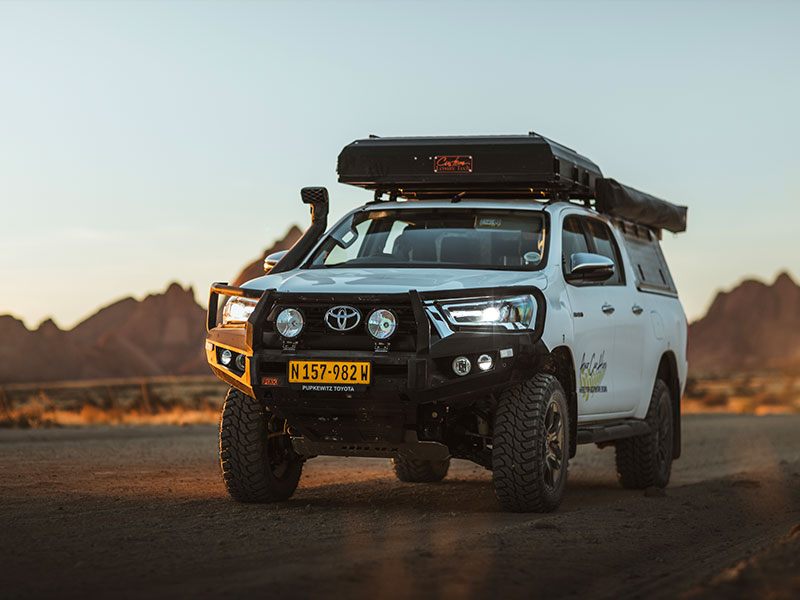 Asco Car Hire Huurauto voor een self-drive-reis op een stoffige weg in Namibi&euml; bij zonsondergang